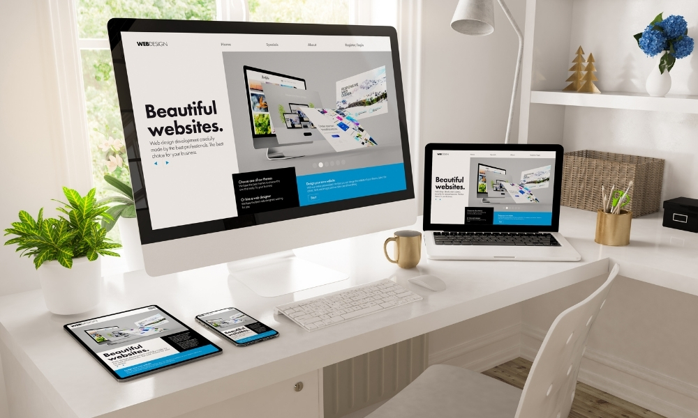 A clean white desk with multiple devices (desktop, laptop, tablet, phone) displaying responsive custom built websites.