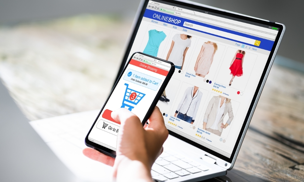 A person viewing an online clothing store on a laptop and adding an item to a cart on a smartphone. This illustrates the importance of responsive design for custom built websites.